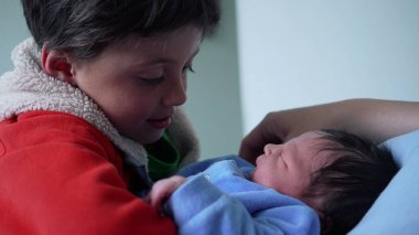 Mavi elbiseli, yeni doğmuş bebeği nazikçe kucaklayan genç çocuk, duygusal ve hassas aile anı, kardeş bağı, sevgi ve yeni bir aile üyesine hoş geldin demenin sevinci