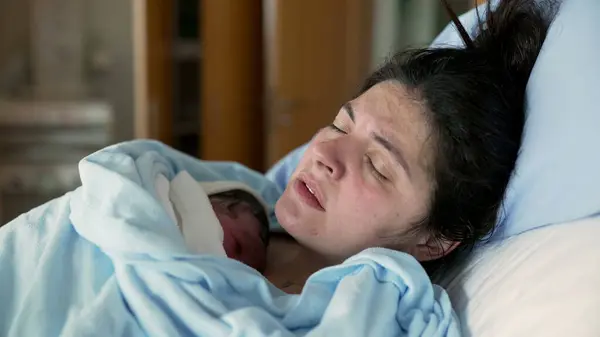 Hastane kliniğinde doğum sonrası travma geçiren yeni anne göğsünde yeni doğan bebeği tutuyor. Doğumdan sonra acı çeken kadın, gerçek hayatta insan mücadelesinin otantik duygusu.