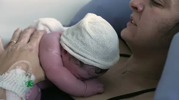 Doğum anı. Yeni doğan bebeğin annesinin göğsünde dinlenen gerçek doğum anı. Anne ve bebek arasındaki ten temasını vurgulamak.