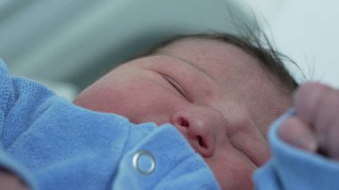 Mavi tulumlu yeni doğmuş bir bebeğin gözleri kapalı bir şekilde huzurlu bir şekilde uyuması. Yumuşak cilt ve gevşek ifade, çocukluk döneminin huzurlu ve hassas anlarını vurgular.