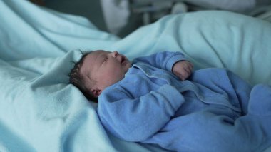 Mavi tulumlu güzel bir bebek, hastane yatağında derin bir uykuya dalmış, yumuşak mavi battaniyelere sarılmış, yeni doğan bakımının huzurlu ve hassas anları ve erken aile hayatı.