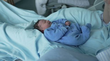 Mavi tulumlu güzel bir bebek, hastane yatağında derin bir uykuya dalmış, yumuşak mavi battaniyelere sarılmış, yeni doğan bakımının huzurlu ve hassas anları ve erken aile hayatı.
