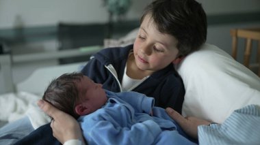 Küçük çocuk, doğumdan sonra bebek kliniğinde ilk gününde yeni doğan erkek kardeşiyle etkileşime giriyor.