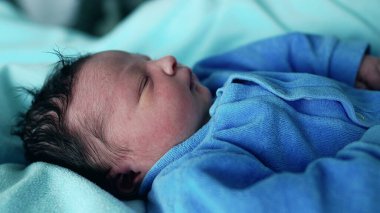 Yeni doğmuş bebek, mavi bir battaniyenin üzerinde uyur, ilk günlerdeki sükuneti ve masumiyeti yakalar. Yumuşak mavi bir kıyafet içinde, bebek sakin bir atmosferle çevrili, gözleri kapalı dinleniyor.