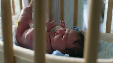 Yeni doğmuş bebek beşiğin içinde huzur içinde, beşik parmaklıklarından görünür, erken yaşların huzurlu ve nazik anlarını yakalar, rahat bir ortamda doğan bir bebeğin masumiyetini ve sükunetini vurgular.