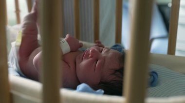 Yeni doğmuş bebek beşiğin içinde huzur içinde, beşik parmaklıklarından görünür, erken yaşların huzurlu ve nazik anlarını yakalar, rahat bir ortamda doğan bir bebeğin masumiyetini ve sükunetini vurgular.