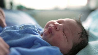 Yeni doğan bebek huzur içinde uyuyor mavi tulum giyiyor, bebeğin yüzüne odaklanıyor. Huzurlu bir ifade, yeni doğmuş bir bebeğin masumiyetini ve huzurunu ön plana çıkarır.