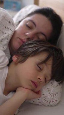 Bir anne ve çocuğun huzurlu bir şekilde yatakta kucaklaşması, yüzleri rahat ve huzurlu, paylaşılan dinlenme ve güvenlik anlarının sükunetini ve huzurunu gösteriyor.