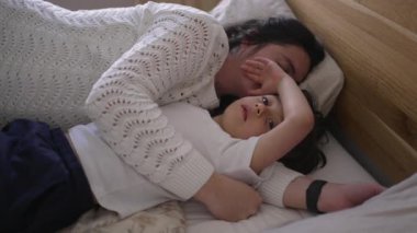 Anne ve küçük çocuk yatakta yatıyor, anne başını çocuğun göğsüne yaslıyor, huzurlu ve samimi bir aile anını yakalıyor, aile sevgisini ön plana çıkaran yaşam tarzı için mükemmel.
