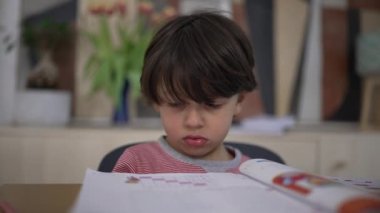 Genç çocuk, okul aktivitelerinden gözle görülür şekilde hayal kırıklığına uğramış ama yine de kararlı. Çalışmasını tamamlamak için bir kalem alıyor, direnç gösteriyor ve zorluklara rağmen öğrenmeye odaklanıyor.