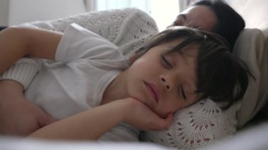 Anne ve çocuk yatakta huzur içinde uyuyor, yüzleri rahat ve huzurlu, rahat bir ortamda hassas ve rahatlatıcı bir dinlenme anı yakalıyorlar.