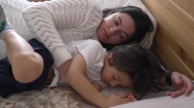 Anne ve çocuk yatakta huzur içinde uyuyor, huzurlu ve samimi bir dinlenme ve kaynaşma anı yakalıyorlar, paylaştıkları sevgi ve rahatlığı vurguluyorlar.