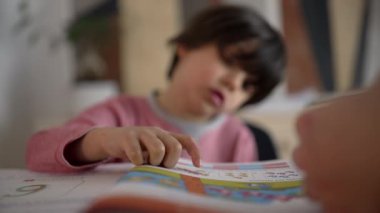 Çocuğun renkli bir kitap okuyup ebeveyn rehberliği yapması, konsantrasyonu vurgulaması ve destekleyici bir ev ortamında öğrenmenin verdiği keyfi vurgulaması.