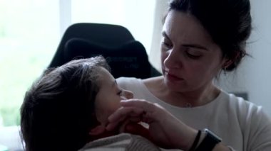 Anne incinmiş çocuğunu rahatlatıyor, endişeli hissediyor, çocuk kollarında dinleniyor, onu daha rahat hissettirmeye çalışıyor, duygusal bir an, yuva kurmak, destekleyici ve ilgili bir etkileşim, kapalı alanda.