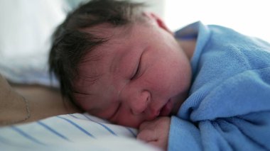 Yeni doğmuş bir bebeğin mavi bir battaniyeye sarılıp anne-baba ve çocuk arasındaki samimiyet ve bağın resmedildiği bir bebeğin yakın çekimi. Yeni doğan bakımı ve aile teması için ideal