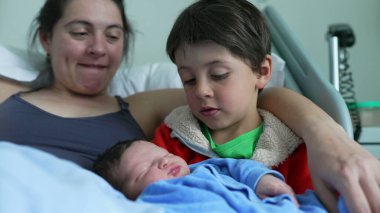 Mother watches lovingly as older sibling cradles newborn baby, highlighting the tender bonds of family love, affection, and the nurturing connection between siblings in a heartfelt moment clipart