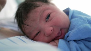 Mavi tulumlu bir bebeğin yan profili, merak ve merakla bakıyor, keşfin ilk anlarını yakalıyor ve yumuşak ve huzurlu bir ortamda yeni bir hayatın masumiyetini yakalıyor.