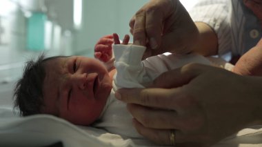 Yeni doğmuş bir bebek, hastanede şefkatli ellerle beyaz tulum giyer, doğumdan hemen sonra yeni doğanlara gösterilen hassas ve hassas ilgiyi gösterir.