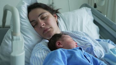 Mother and newborn baby sleeping together in a hospital bed, both in matching blue outfits, capturing the serene and tender moments of early bonding and the comfort of a shared rest