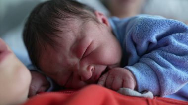 Mavi tulumlu yeni doğmuş bir bebeğin, büyük bir kardeşin göğsünde dinlenmesi, sevgi dolu ve huzurlu bir aile ortamında güçlü bir kardeş bağı sergilemesi.