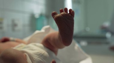 Close-up of newborn baby foot raised in the air, lying on hospital bed, wearing diaper, showing tiny toes and delicate skin, symbolizing new beginnings and life