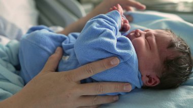 Yeni doğmuş bebek mavi bir tuluma sarılmış, ebeveyn tarafından nazikçe tutuluyor, yaşamın ilk aşamalarında gösterilen yakınlık ve şefkatli ilgiyi gösteriyor, sevgi ve güvenliği vurguluyor.