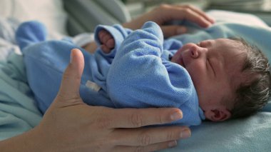 Yeni doğmuş bebek mavi bir tuluma sarılmış, ebeveyn tarafından nazikçe tutuluyor, yaşamın ilk aşamalarında gösterilen yakınlık ve şefkatli ilgiyi gösteriyor, sevgi ve güvenliği vurguluyor.