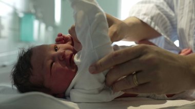 Yeni doğmuş bir bebek, hastanede şefkatli ellerle beyaz tulum giyer, doğumdan hemen sonra yeni doğanlara gösterilen hassas ve hassas ilgiyi gösterir.