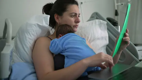 stock image New mother in hospital bed reviewing documents while holding sleeping newborn, multitasking between paperwork and parenting, healthcare setting, postnatal care, balancing family and responsibilities