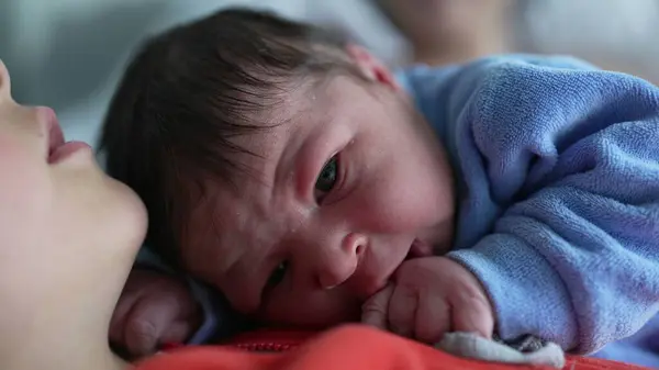 stock image Close-up of a newborn baby in a blue onesie resting on an older sibling's chest, showcasing the tender moment and the strong sibling bond in a loving and serene family environment