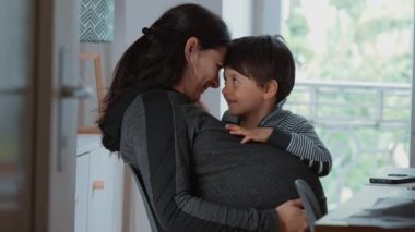 Hamile bir kadın, gerçek bir hayat sahnesinde anne ile oğlu arasındaki bağı vurgulayarak, samimi ve neşeli bir şekilde küçük çocuğuna sarılıp gülüyor.