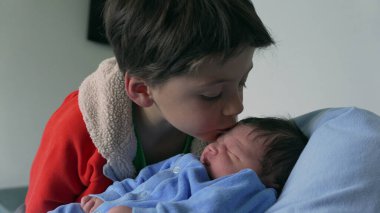Genç çocuk sevgiyle yeni doğan kardeşini kucaklıyor, mavi giyinmiş, hassas anı yakalıyor ve aile bağını kuvvetlendiriyor, sevgi, aile ve yeni doğan bebeğe kucak açmanın sevinci için ideal.