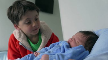 Genç çocuk sevgiyle yeni doğan kardeşini kucaklıyor, mavi giyinmiş, hassas anı yakalıyor ve aile bağını kuvvetlendiriyor, sevgi, aile ve yeni doğan bebeğe kucak açmanın sevinci için ideal.