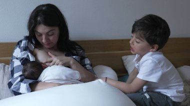 Annem yeni doğmuş bebeği emzirirken abim izliyor. Sevgi ve ilgiyle dolu bir aile anını sergiliyorum.