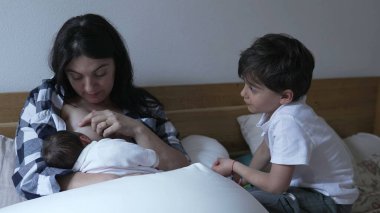 Annem yeni doğmuş bebeği emzirirken abim izliyor. Sevgi ve ilgiyle dolu bir aile anını sergiliyorum.