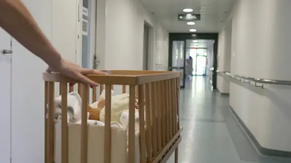 stock image Hand pushing a crib with a newborn baby down a hospital corridor, illustrating the first week of newborn care, ideal for family, parenting, and healthcare