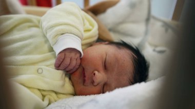 Yeni doğmuş bir bebeğin rahat sarı tulumuyla yakın çekimde mışıl mışıl uyuyor. Bebekliğin yumuşak ve huzurlu doğasını, aile ve sağlık hizmetleri için ideal olduğunu vurguluyor.