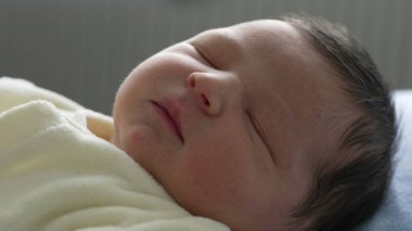 Yeni doğmuş bebek sakin bir ifadeyle uyuyor, yumuşak sarı bir battaniyeye sarılmış. Bebeğin dingin yüzüne odaklanarak, bebekliğin sükunetini ve saflığını vurguluyor.