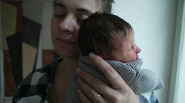 Yeni doğmuş bebeğini kucaklayan bir annenin yakın çekimi, bu samimi anda paylaşılan sevgi ve şefkati gösteriyor.