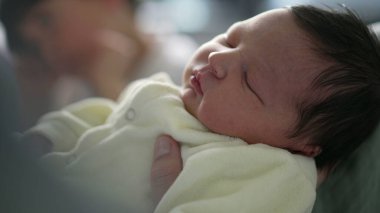 Yeni doğmuş bir bebeğin battaniyeye sarılı uyuduğu yakın plan. Bebeğin huzurlu ifadesi ve yumuşak battaniyesi, uyuyan bir bebeğin sükunetini vurgulayan sıcak ve rahatlatıcı bir sahne yaratır.