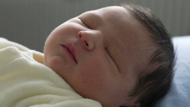 Yeni doğmuş bebek sakin bir ifadeyle uyuyor, yumuşak sarı bir battaniyeye sarılmış. Bebeğin dingin yüzüne odaklanarak, bebekliğin sükunetini ve saflığını vurguluyor.