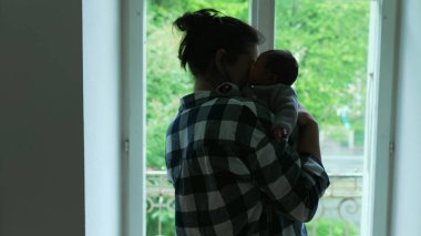 Anne sevgiyle yeni doğmuş bebeğini kucağına alıyor, bu samimi aile anındaki yakınlık ve sevgiyi vurguluyor.