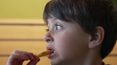 Çocuk gevrek bir patates kızartmasının tadını çıkarıyor, gözleri heyecan içinde gevrek bir yemek atmosferinde gevrek dokusunun ve tadının tadını çıkarıyor.