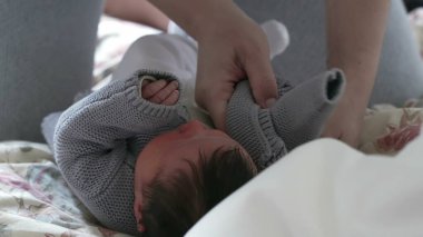 Ebeveynler yeni doğan bir bebeğe rahat gri bir süveter giydirip, bebeklere gösterdikleri özeni ve sevgi dolu ilgiyi resmediyor ve erken çocukluktaki ebeveynlerin yetiştirme sorumluluklarını vurguluyor.