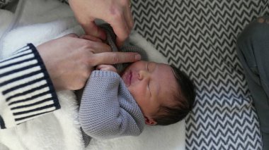 Bebek rahatsız görünürken annenin eli örgü örülmüş gri bir kıyafetin kolundan nazikçe yeni doğan bebeğin elini çekiyor. Hassas bir bakım ve uyum anı
