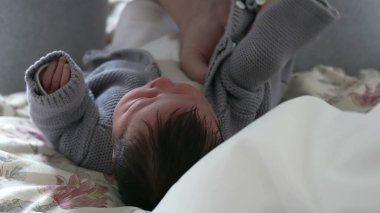 Ebeveynler yeni doğan bir bebeğe rahat gri bir süveter giydirip, bebeklere gösterdikleri özeni ve sevgi dolu ilgiyi resmediyor ve erken çocukluktaki ebeveynlerin yetiştirme sorumluluklarını vurguluyor.