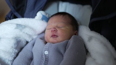 Yeni doğmuş bebek rahat bir battaniyenin içinde uyur, yumuşak, örülü bir kazak giyer, hayatın ilk zamanlarının huzurunu yakalar.