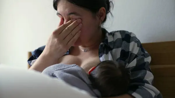 stock image Mother breastfeeding baby while feeling tired, capturing the challenges and reality of breastfeeding, emphasizing the strength and dedication of mothers in nurturing their children