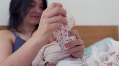 Anne, yeni doğmuş bebeğini kucağında tutarken yürekten bir hediyeyi açıyor. Merakla izliyor, samimi bir aile anı. Sevgiye, kaynaşmaya, ev yapımı reçele vurguluyor.
