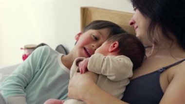 Anne, büyük kardeş bakarken bebeğini kucaklar ve şefkatli bir aile anı yaratır. Büyük çocuklar bebeğe bakıyorlar. Bu samimi sahnede merak ve kardeşlik bağı oluşuyor.